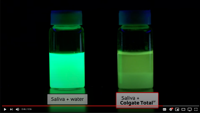 two testing tubes placed in a dark room comparing the reaction to water and Colgate on saliva