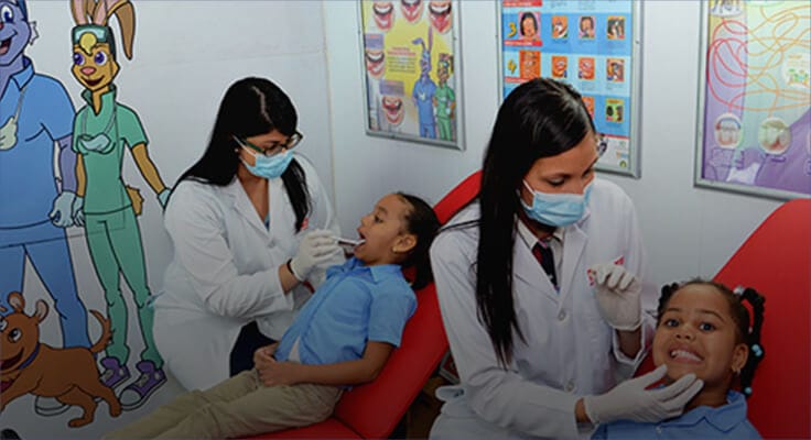 children smiling while sitting on a dental chair as dental hygienist look at their teeth 