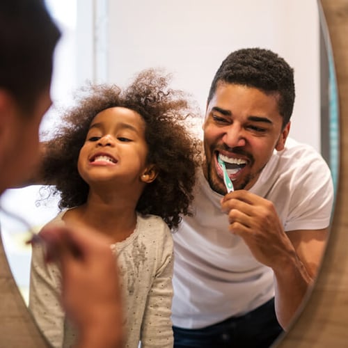Father and daughter looking at mirror while brushing teeth