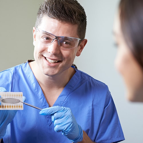 Dentist wearing glasses and gloves showing patient a teeth chart 