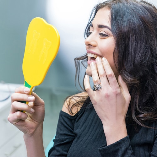 Woman looking at her teeth with a yellow hand-held mirror 