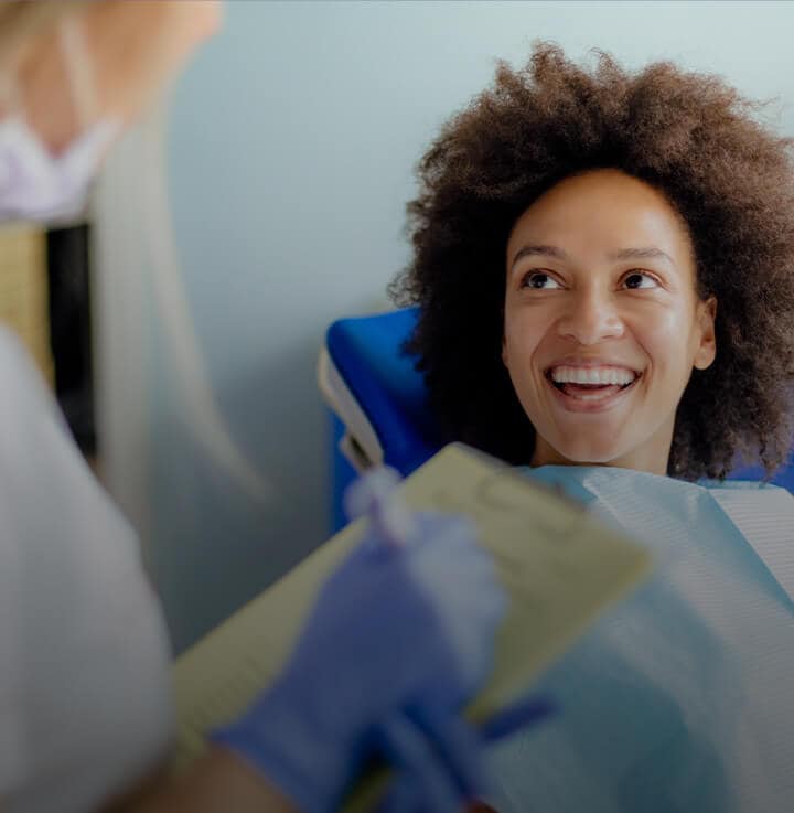 woman with big curly hair sitting on a dentist chair and smiling