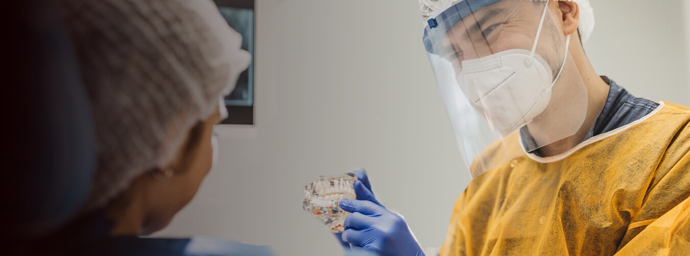 A dental professional wearing safety PPE gear and white lab coat smiling compassionately