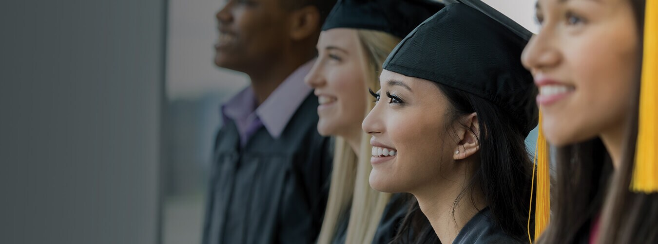 students in smiling while wearing black cap and gowns at a graduation ceremony